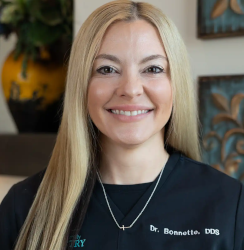 Dr. Carly Bonette smiles in a black branded top, presenting a friendly and professional appearance in a dental office setting.